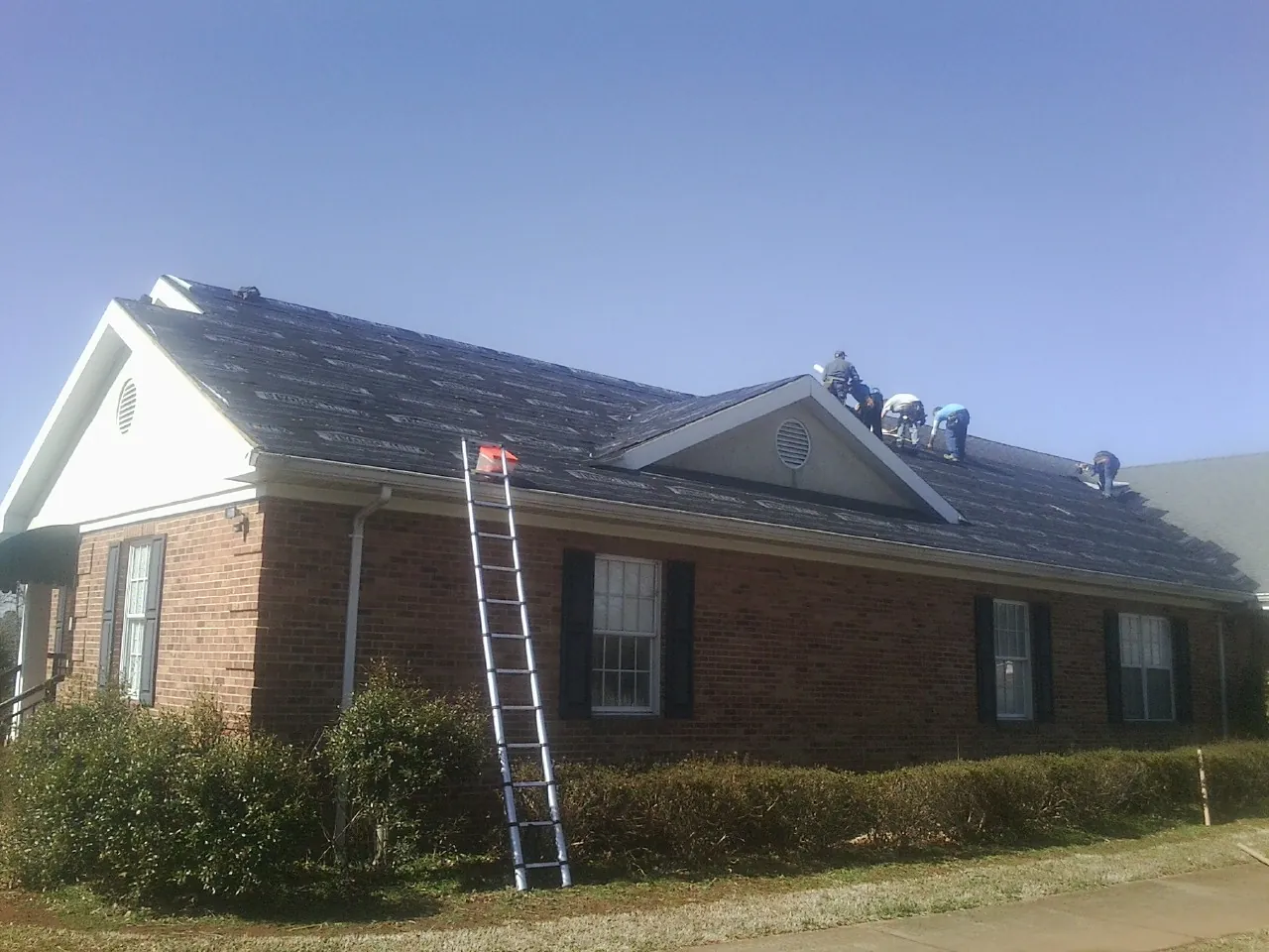 Crew tearing shingles off a brick ranch roof with a ladder set — Emergency Roof Repair work by our crew in Guysville