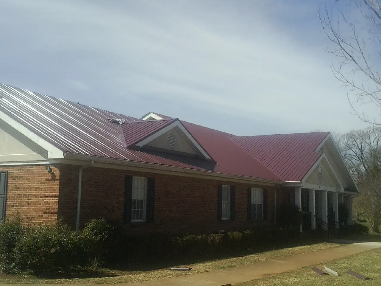 Red metal roof with gabled entries on a long brick building, from a Hail Damage Roof Repair job in Guysville