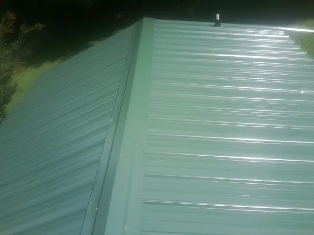 New green metal panels meeting at the ridge of a roof — Flat Roof Repair work by our crew in Guysville