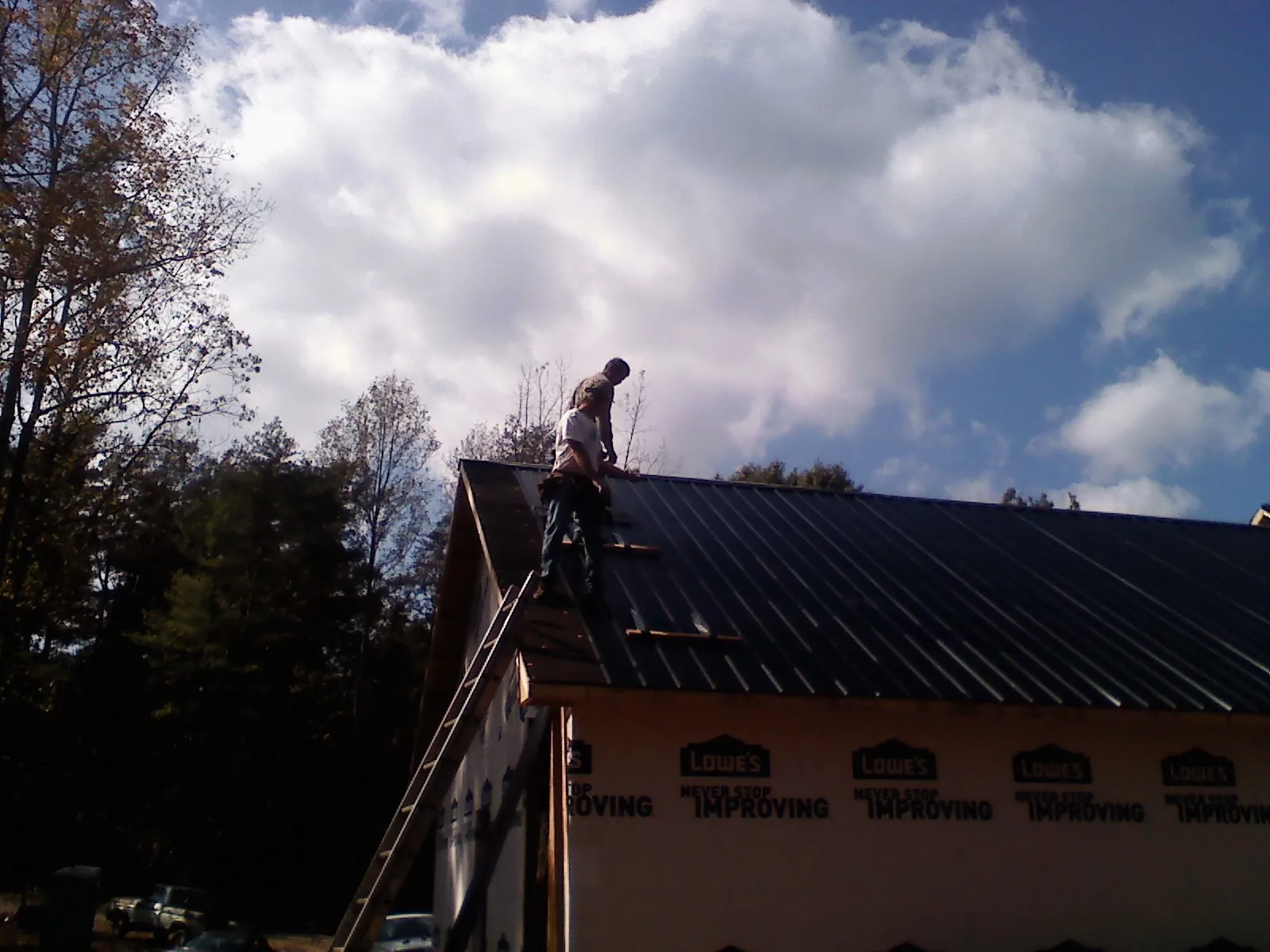 Roofer fastening dark metal panels high against a cloudy sky, from a Roof Inspection job in Guysville
