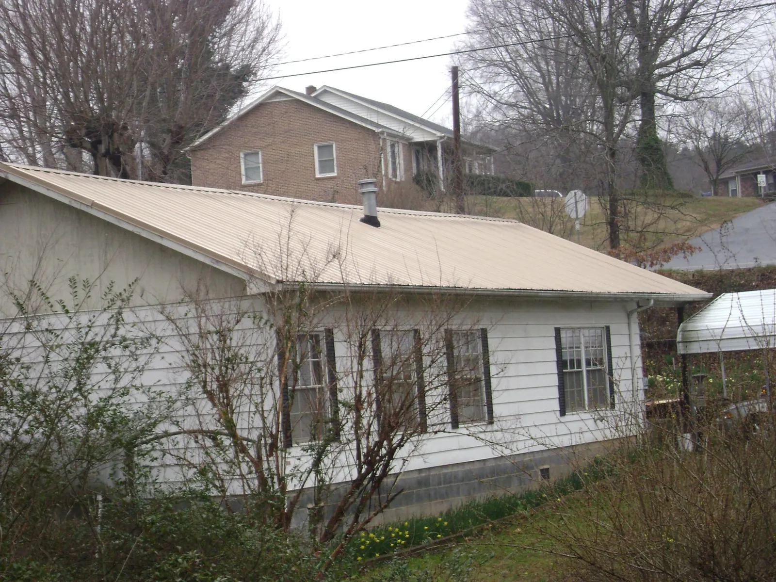 Tan metal roof on a white sided house set into a hillside — Commercial Roofing by Roofing Brothers in Guysville